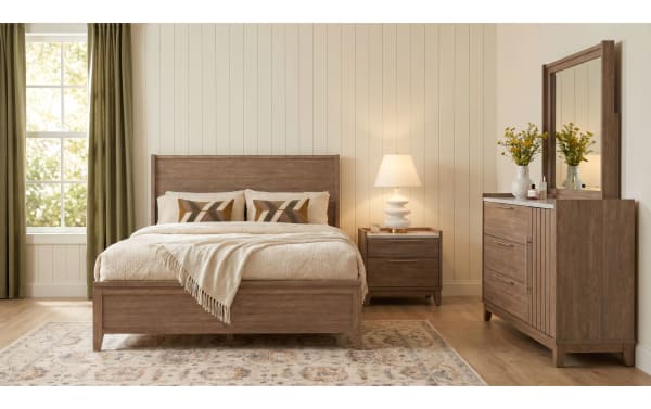Modern bedroom with wooden bed frame, beige bedding, matching nightstand with lamp, and dresser with mirror and floral decor.